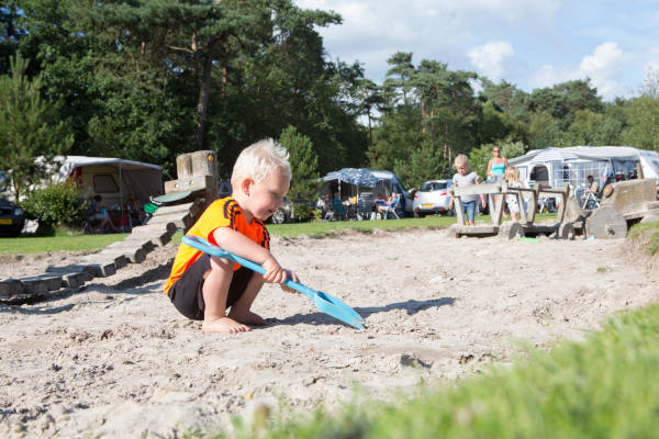 Jongen is aan het spelen in het zand met een schepje