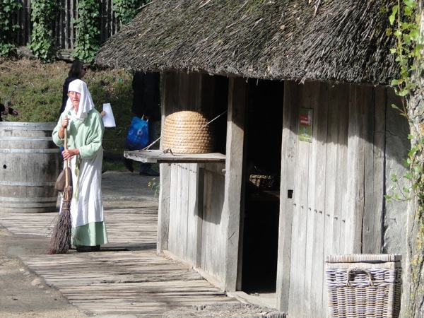 Een vrouw uit de late middeleeuwen veegt haar stoep in het Archeon