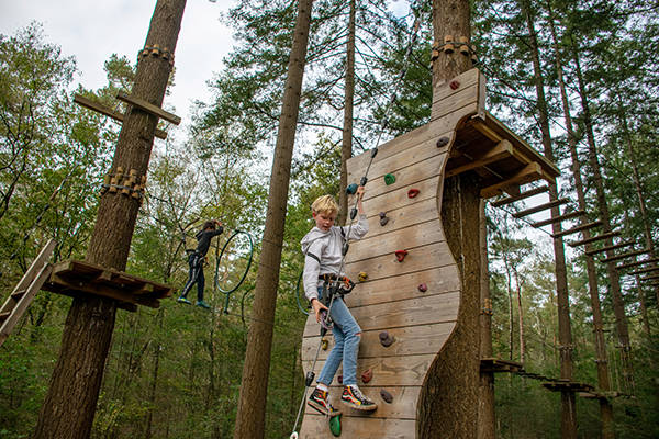  Jongen loopt op klimmuur op de klimroute in het bos