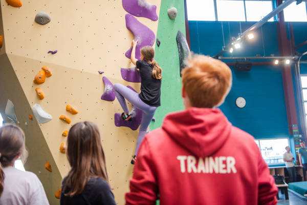 Meisje wordt begeleid door trainer tijdens het boulderen